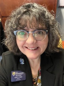 Woman with glasses, black jacket and UNCG name tag.